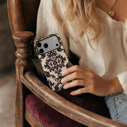 Burgundy Damask matte case on iPhone 17 Pro Max, styled with vintage dark wood and a minimalist brass compass on a clean studio surface.